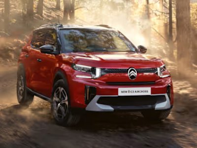 Red Citroën Ë-C3 Aircross driving on a dirt path in a forested area.