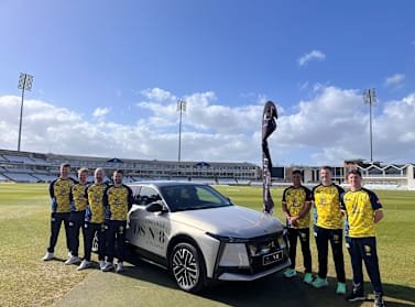 T20 Durham Cricket team members standing beside a DS No.8 on a stadium field.