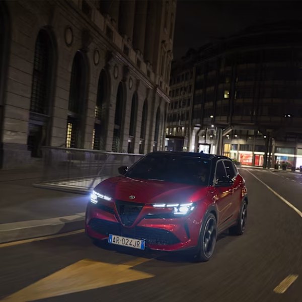 Red Alfa Romeo driving through a Gateshead urban street at night, under city lights to a garage