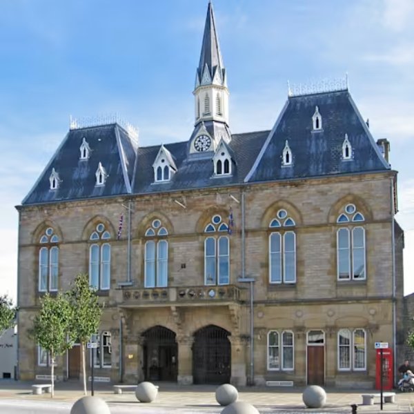 Historic Bishop Auckland Town Hall with clock tower and arched windows under a clear sky.
