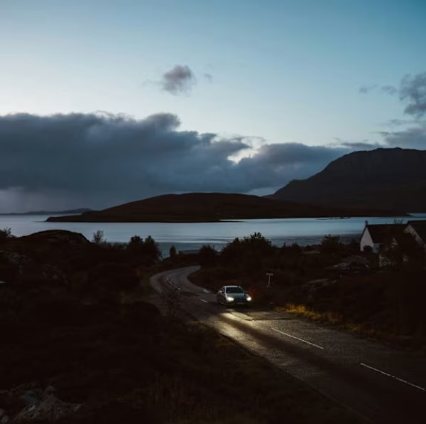 Car with headlights on a Hartlepool winding road near a lake at dusk.