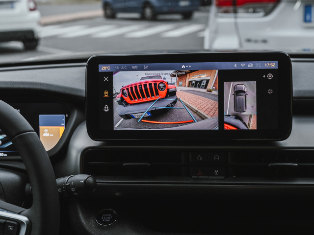Car dashboard showing an external camera view of another vehicle on the display screen.
