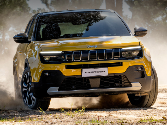 Yellow Jeep Avenger SUV driving on a dirt road, kicking up dust.