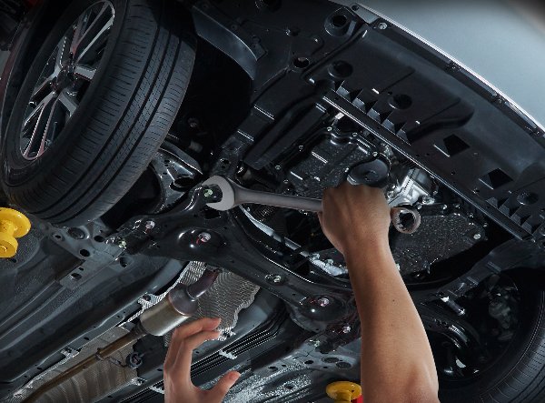 Mechanic Repairing Car Undercarriage with Wrench in Auto Service Workshop