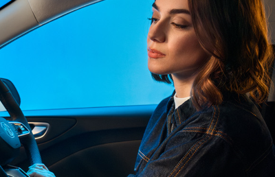 Person seated in a car, looking downwards with hands on the steering wheel.