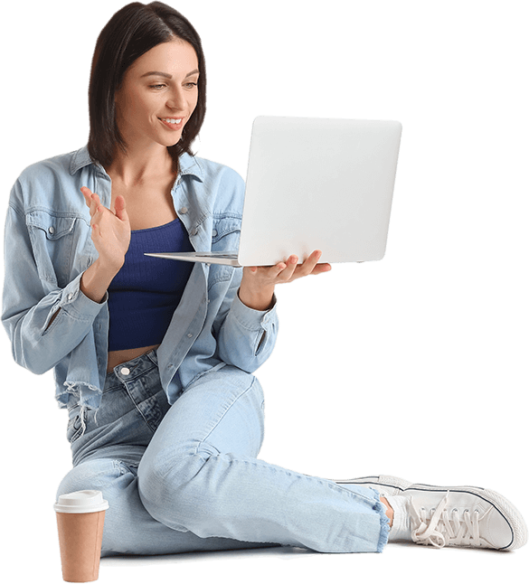 Woman in denim outfit sitting with laptop, waving.